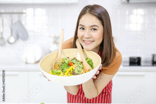 A young Asian woman making salad in a modern kitchen.