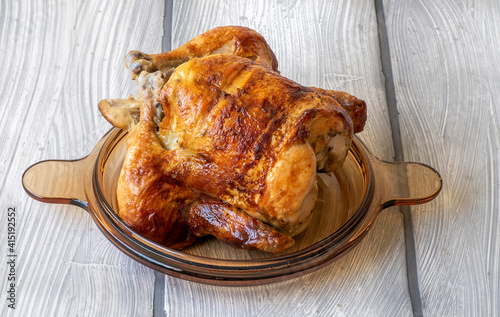 Homemade tasty rotisserie chicken on white wooden surface. photo