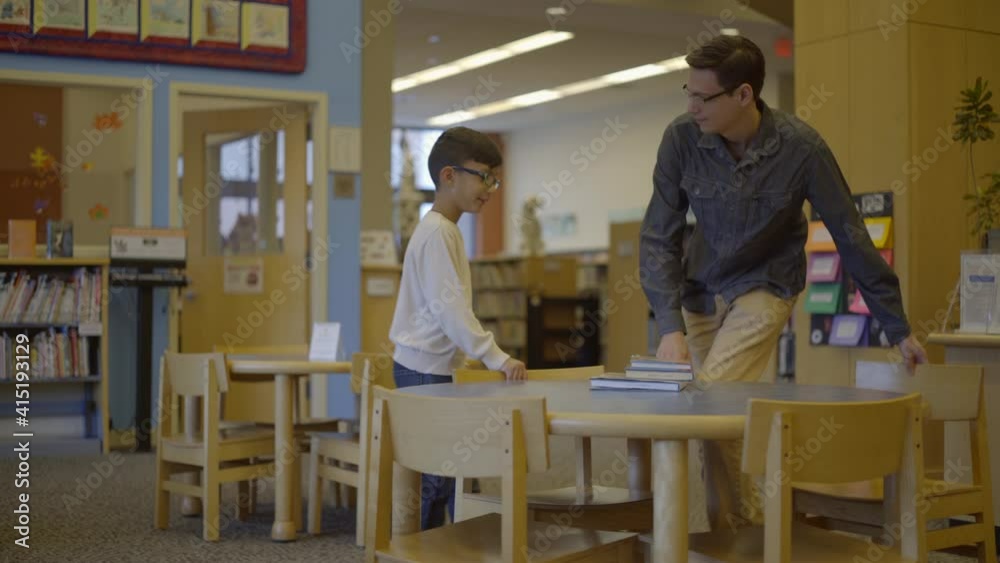 Young Father and Son at the Library Sit Down at a Table Young Father and Son at the Library Sit Down at a Table