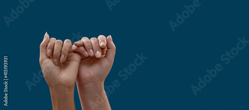 Two hands hook each other little finger pinkie as a symbol of promise or pardon isolated on blue background