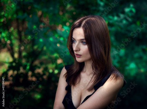Beautiful brunette girl with blue eyes in the forest. Witching look. Sun spots and glare. Effective bokeh. Selective focus. Blurred background.