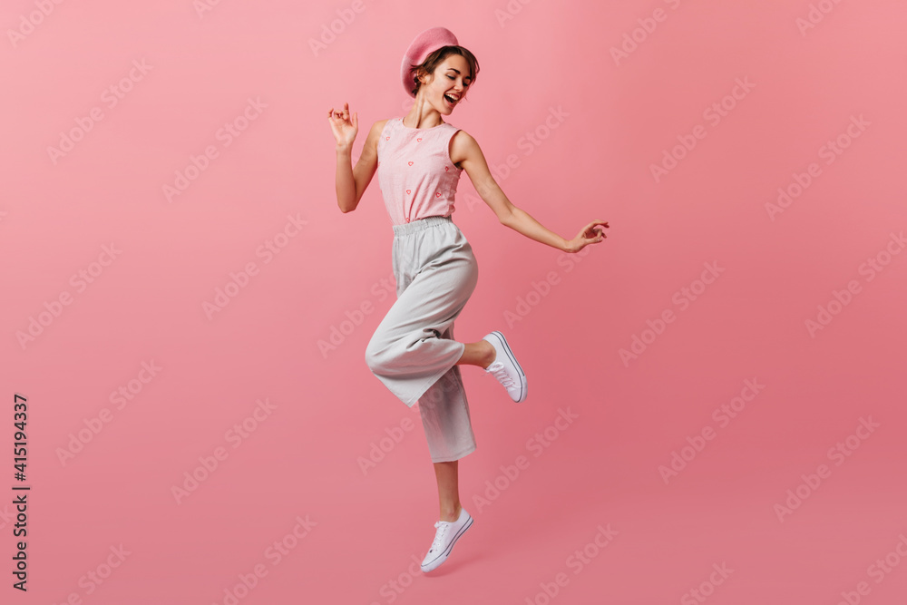 Full length view of dancing caucasian lady in pants. Refined french girl in beret having fun on pink background.
