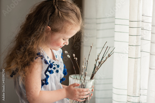 Cute little girl with long curly hair sits by the window with pussy willow branches photo