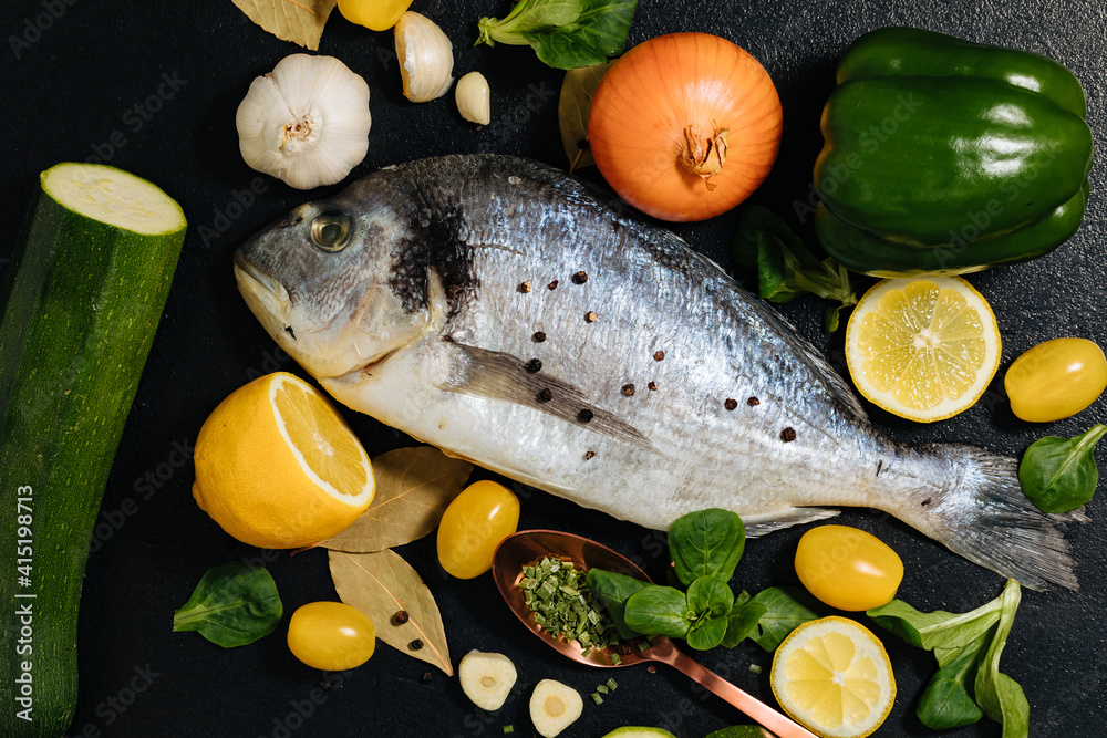 fish with lemon and vegetables. Delicious fresh fish on black dark background. Fish with aromatic herbs, spices and vegetables on a black table. healthy food, diet, cooking concept. Prepare fish fish with lemon and vegetables. Delicious fresh fish on black dark background. Fish with aromatic herbs, spices and vegetables on a black table. healthy food, diet, cooking concept. Prepare fish