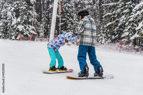 The father teaches his daughter to snowboard