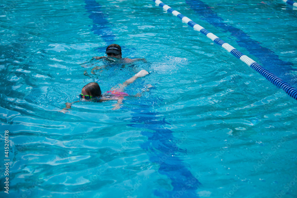 Little girl swimming during her swim lessons at the local outdoor pool in the summer