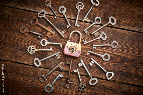 Vintage rusty padlock surrounded by group of old keys on a weathered wooden background. Internet security and data protection concept, blockchain and cybersecurity