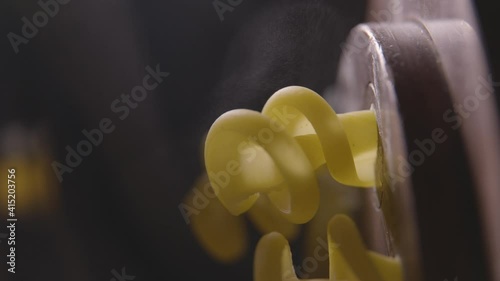 Close-up in slow motion.Professional production of pasta. Pasta dough coming out of the bronze extruder is automatically cut. Steam particles created by the heat in the extruder are visible. 