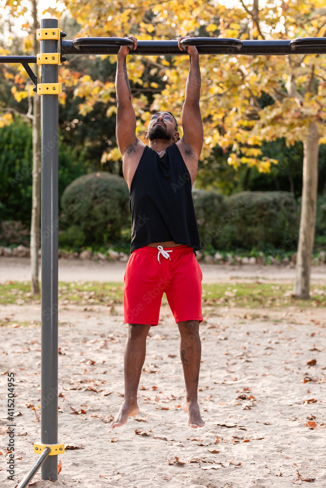 african american athlete boy does calisthenics fitness exercises on bars in park