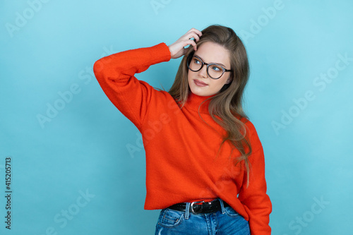 Pretty woman with long hair wearing a casual sweater and glasses over blue background confuse and wonder about question. Uncertain with doubt, thinking with hand on head
