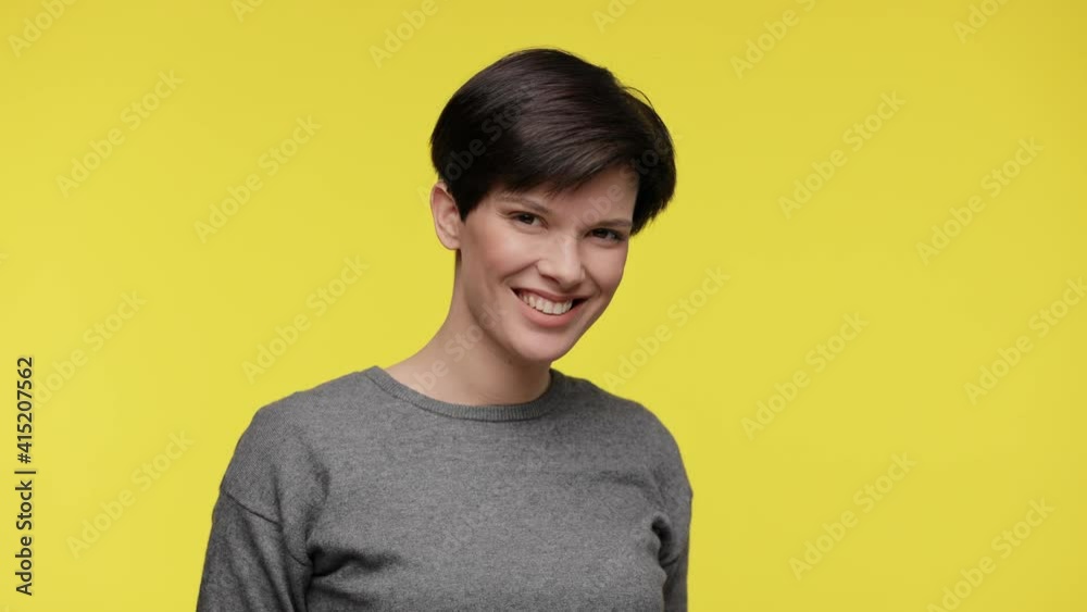 Color of the year 2021. Ultimate Gray and illuminating. Portrait of young smiling beautiful woman wearing gray sweatshirt isolated on yellow background Color of the year 2021. Ultimate Gray and illuminating. Portrait of young smiling beautiful woman wearing gray sweatshirt isolated on yellow background