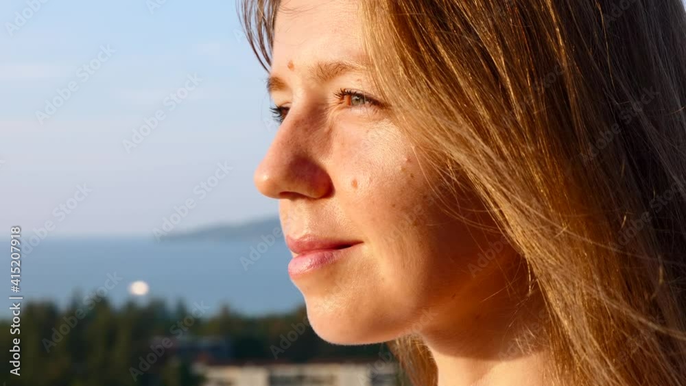 Slow Motion of Young Smiling Woman on Sunset Light and Wind Looking Far Away with Sea and Green Trees on Background. Close Up of Happy Woman Relax on Sunlight, Enjoying Peaceful Sunset Slow Motion of Young Smiling Woman on Sunset Light and Wind Looking Far Away with Sea and Green Trees on Background. Close Up of Happy Woman Relax on Sunlight, Enjoying Peaceful Sunset