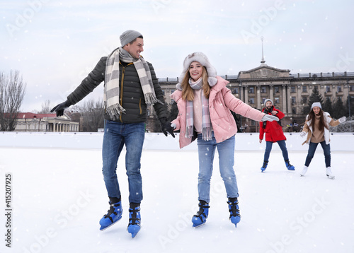 Foto Happy couple with friends skating along ice rink outdoors