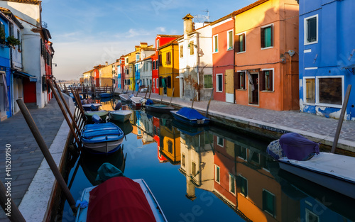 Burano island street at sunset with colorful houses,  boats and reflections in the water