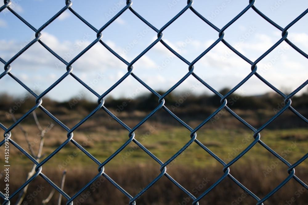 Chain link wire fence close up with blurred foliage in the background, winter, blue sky, UK Chain link wire fence close up with blurred foliage in the background, winter, blue sky, UK