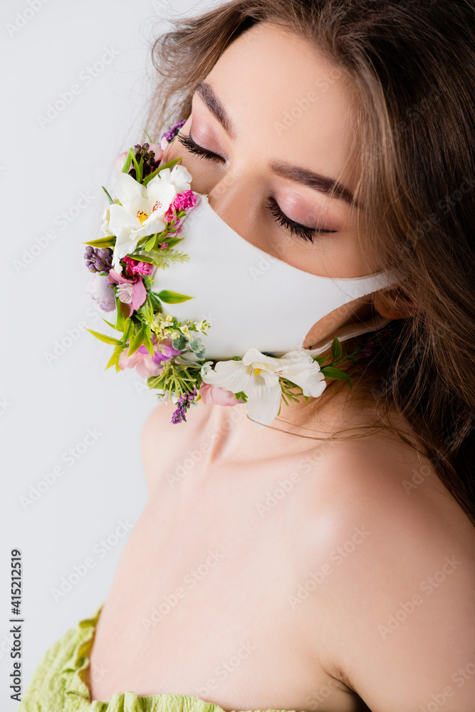 Model with closed eyes and white medical mask with flowers isolated on grey Model with closed eyes and white medical mask with flowers isolated on grey