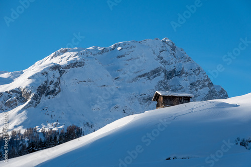 old wooden barn on a snowy slope in front of mountain und blue sky