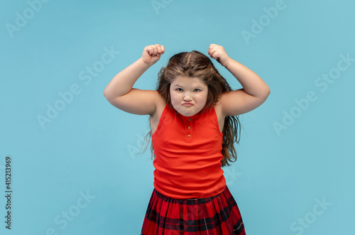 Angry. Happy, smiley little caucasian girl isolated on blue studio background with copyspace for ad. Looks happy, cheerful. Childhood, education, human emotions, facial expression concept.