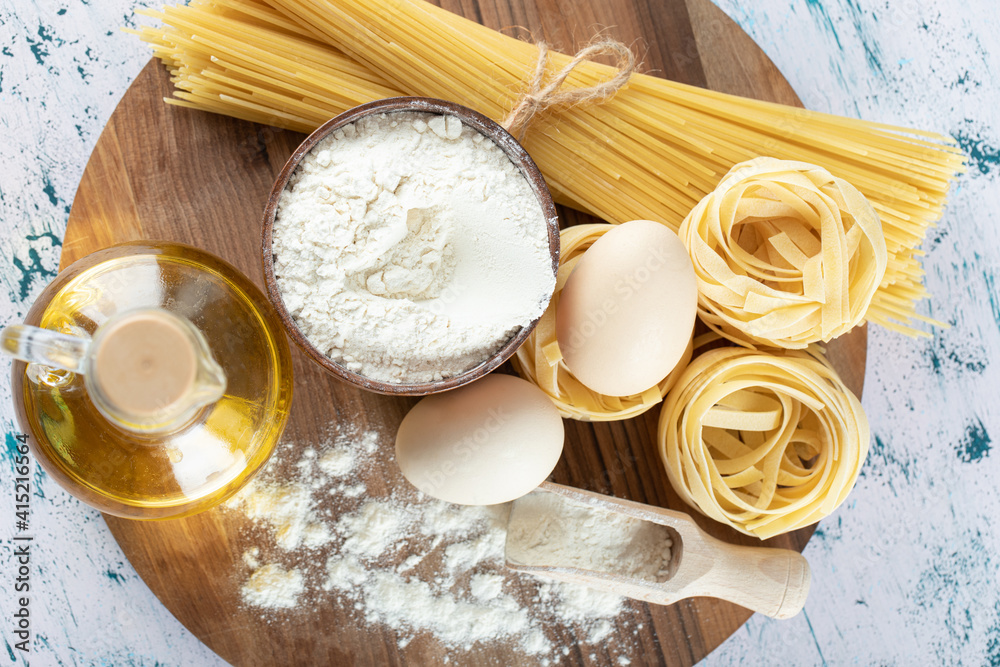 Two kinds raw pasta with oil, egg and bowl of flour on wooden board Two kinds raw pasta with oil, egg and bowl of flour on wooden board