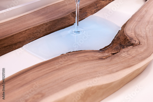 Process making of a craft resin and wood table. Liquid epoxy is poured into a mold with wooden blanks.
