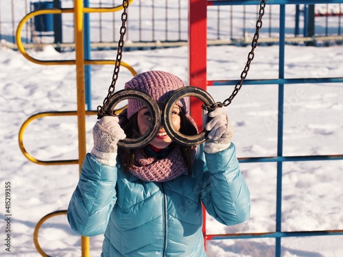Cheerful girl on the playground with gymnastic rings. Sport pasttime. Winter holidays. Winter pastime in the fresh air.