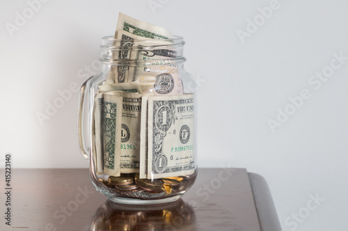 A glass jar filled with bills including USD cash bills and coins in 5 and 1 dollar denominations to display savings photo