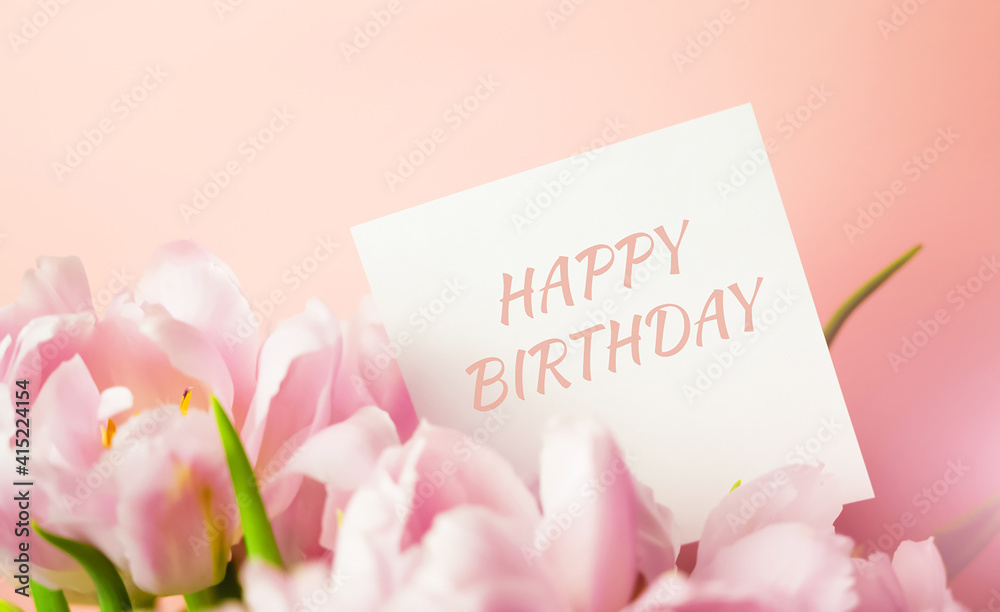 Fototapeta premium A note with Happy birthday text hidden in a bunch of pink tulips. Birthday card