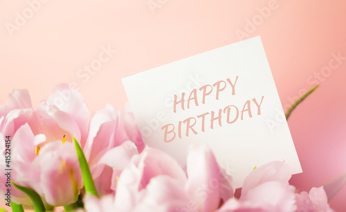 Fototapeta Naklejka Na Ścianę i Meble -  A note with Happy birthday text hidden in a bunch of pink tulips. Birthday card