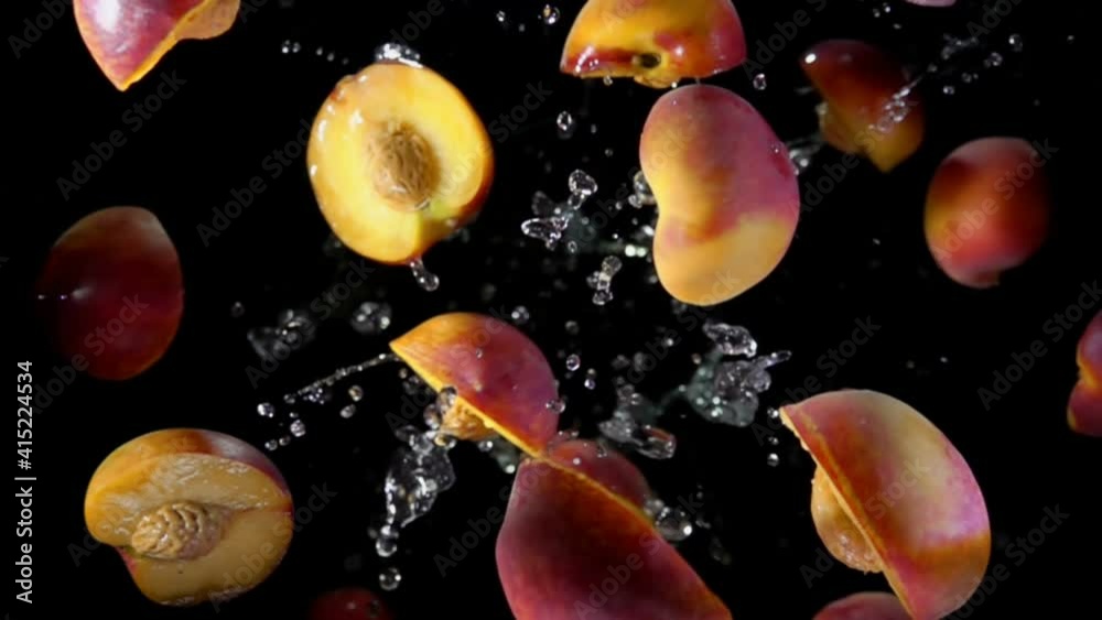 Halves of a wet peach are bouncing in splashes of water on a black background in slow motion