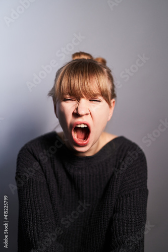 Portrait of young yawning woman wearing black sweater isolated on gray background. Expressions concept
