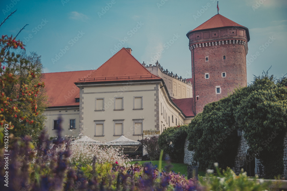 Wawel Senator Tower with castle, green lawns, ivy on the wall, umbrellas and flowers on sunny day. Part of the Wawel royal Castle in Krakow, Poland. Built at the behest of King Casimir III the Great. 