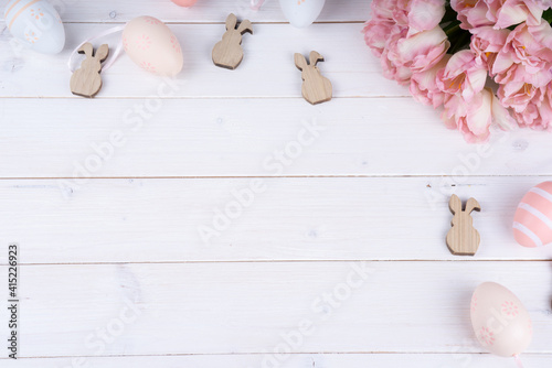 Ostern Bild mit Textfreifläche- Osterhasen, Eier und Blumen auf einem Holzhintergrund. 