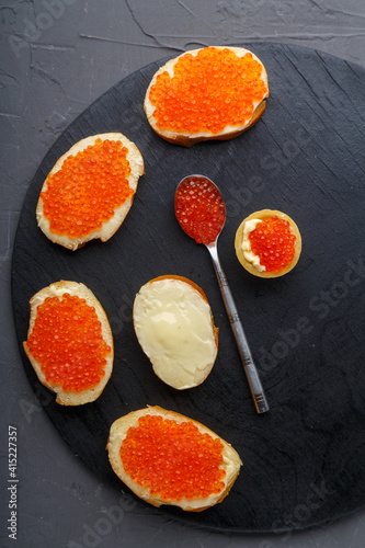 Bruschettes with butter and red caviar on a black board in a row.