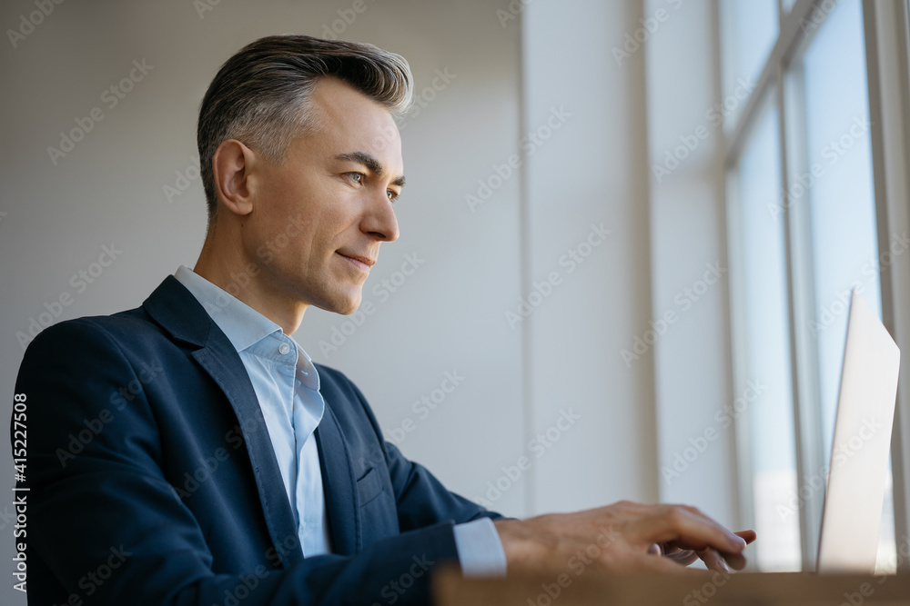 Confident mature businessman using laptop computer, typing, searching online, working in office Confident mature businessman using laptop computer, typing, searching online, working in office