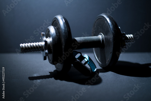 old, dusty dumbbells and fitness tracker on a dark background in the light
