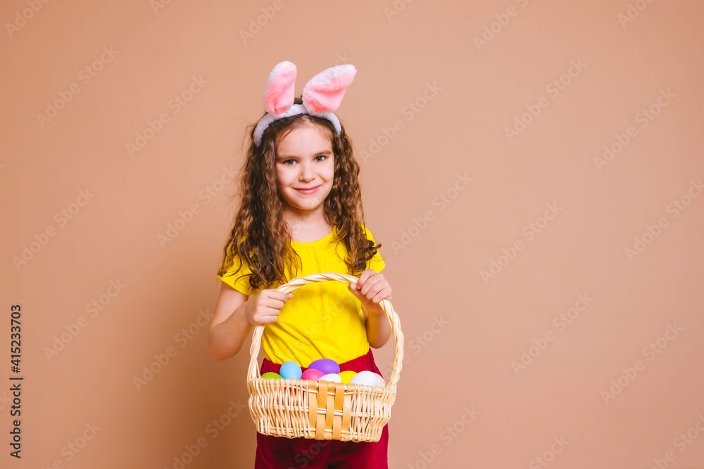Cute girl child with Easter bunny ears holds a basket of colored eggs. Happy Easter, holidays, traditions concept.