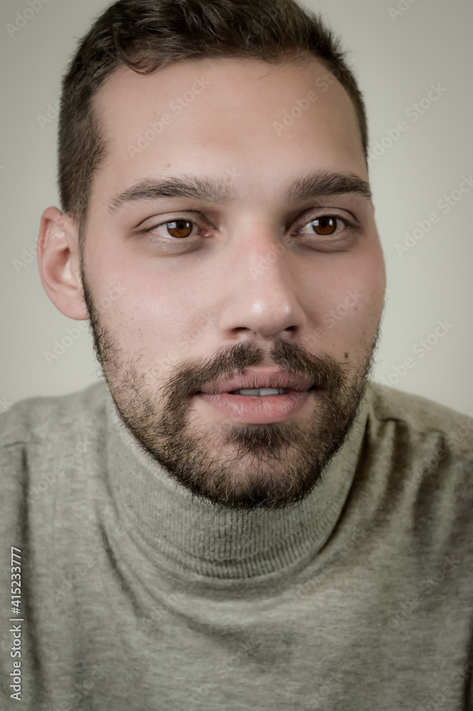 Fototapeta premium Portrait of a young brown-haired man with a short beard and a gray turtleneck sweater
