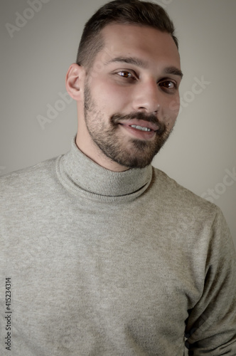 Portrait of a smiling young brown-haired man with a short beard and a gray turtleneck sweater