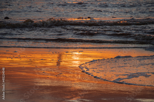 Shoreline of the sea with orange reflection of sunset sky
