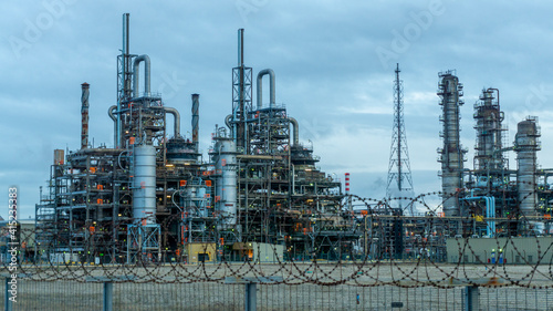 Petroleum Production Plant with Pipes and Tanks and Chimneys with the Security Fence in the Foreground, on an Overcast Day