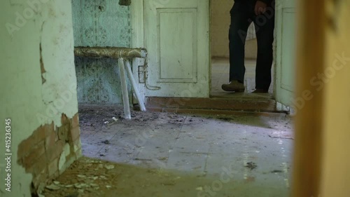 Man dressed in jeans walks on muddy wooden floor of old abandoned village house.