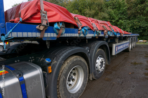 Semi Truck Trailer with a Load of Steel Sheeted with a Tarpaulin and Held in Place with Ropes and Ratchet Straps Half Load