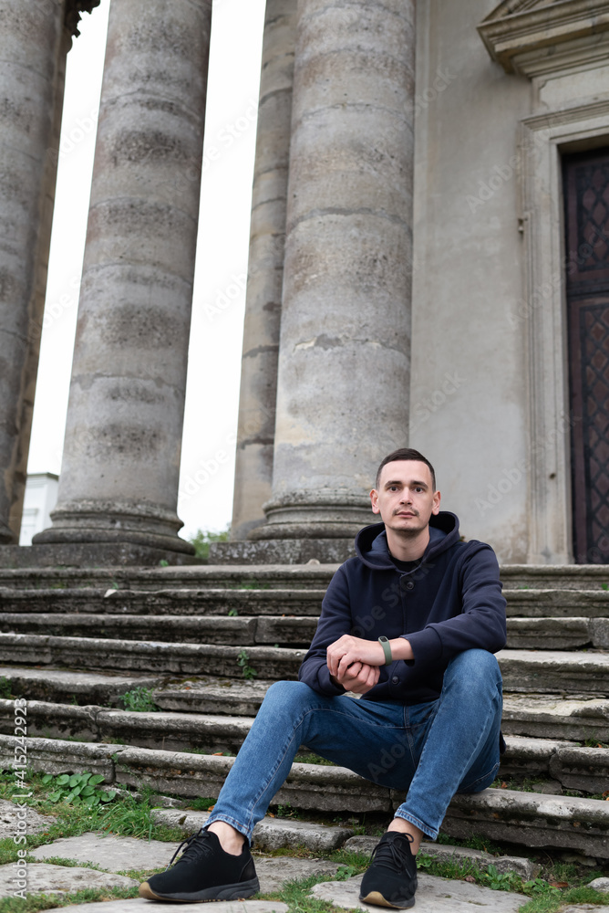 A man sitting on stairs with pillars in the background.