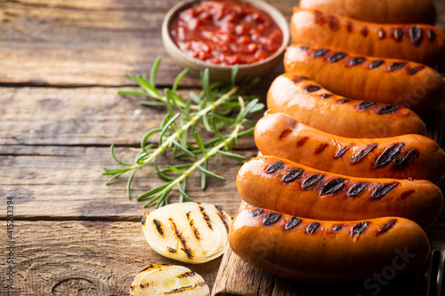 Fried delicious sausages with tomato sauce and herbs on cutting board, wooden background.
