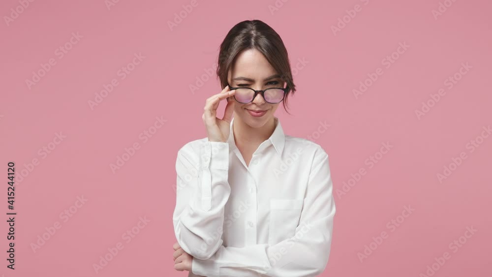 Confident successful business woman 20s in white shirt glasses posing isolated on pink background in studio. Achievement career wealth concept. Straightening collar blinking put hand prop up on chin