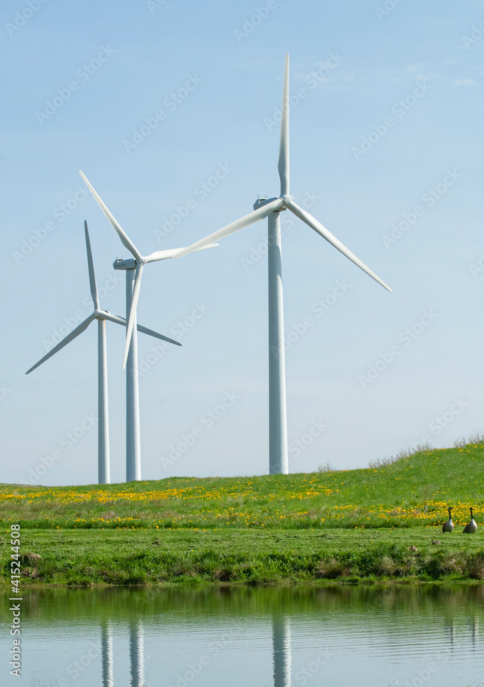 three wind towers rise up from behind a hilltop and reflect into a pond three wind towers rise up from behind a hilltop and reflect into a pond