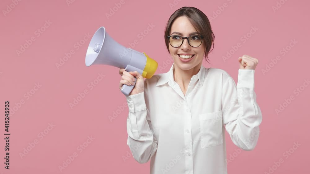 Excited joyful cheerful young business woman in white shirt glasses isolated on pink background studio. Achievement career wealth concept. Screaming in megaphone doing winner gesture clenching fists Excited joyful cheerful young business woman in white shirt glasses isolated on pink background studio. Achievement career wealth concept. Screaming in megaphone doing winner gesture clenching fists