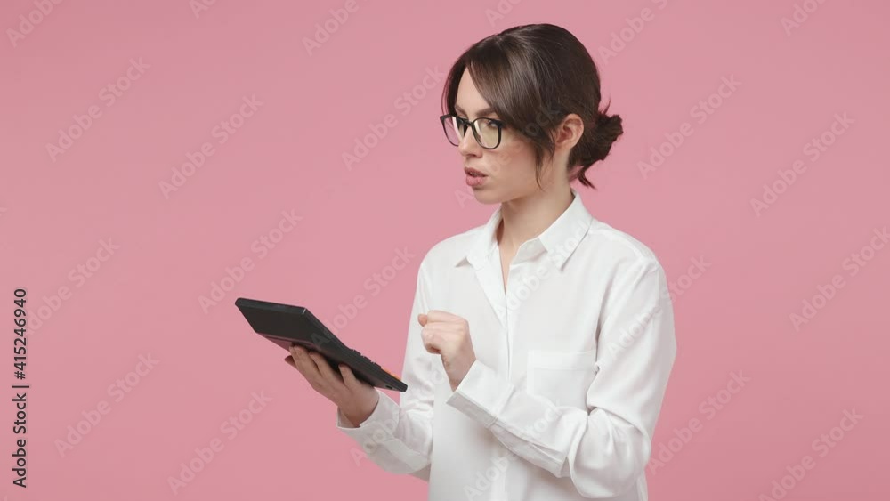 Focused young business woman 20s in white shirt glasses posing isolated on pink background studio. Achievement career wealth concept. Accountant working using calculator showing thumb up like gesture Focused young business woman 20s in white shirt glasses posing isolated on pink background studio. Achievement career wealth concept. Accountant working using calculator showing thumb up like gesture