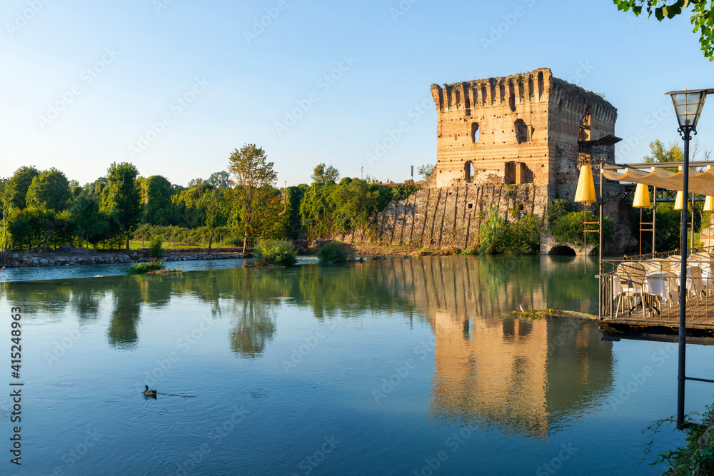 Medieval tower that is reflected in the Mincio river in Valeggio sul Mincio. A local can be glimpsed on a hot summer day, Verona, Veneto, Italy.
