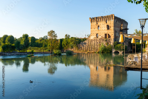 Medieval tower that is reflected in the Mincio river in Valeggio sul Mincio. A local can be glimpsed on a hot summer day, Verona, Veneto, Italy.